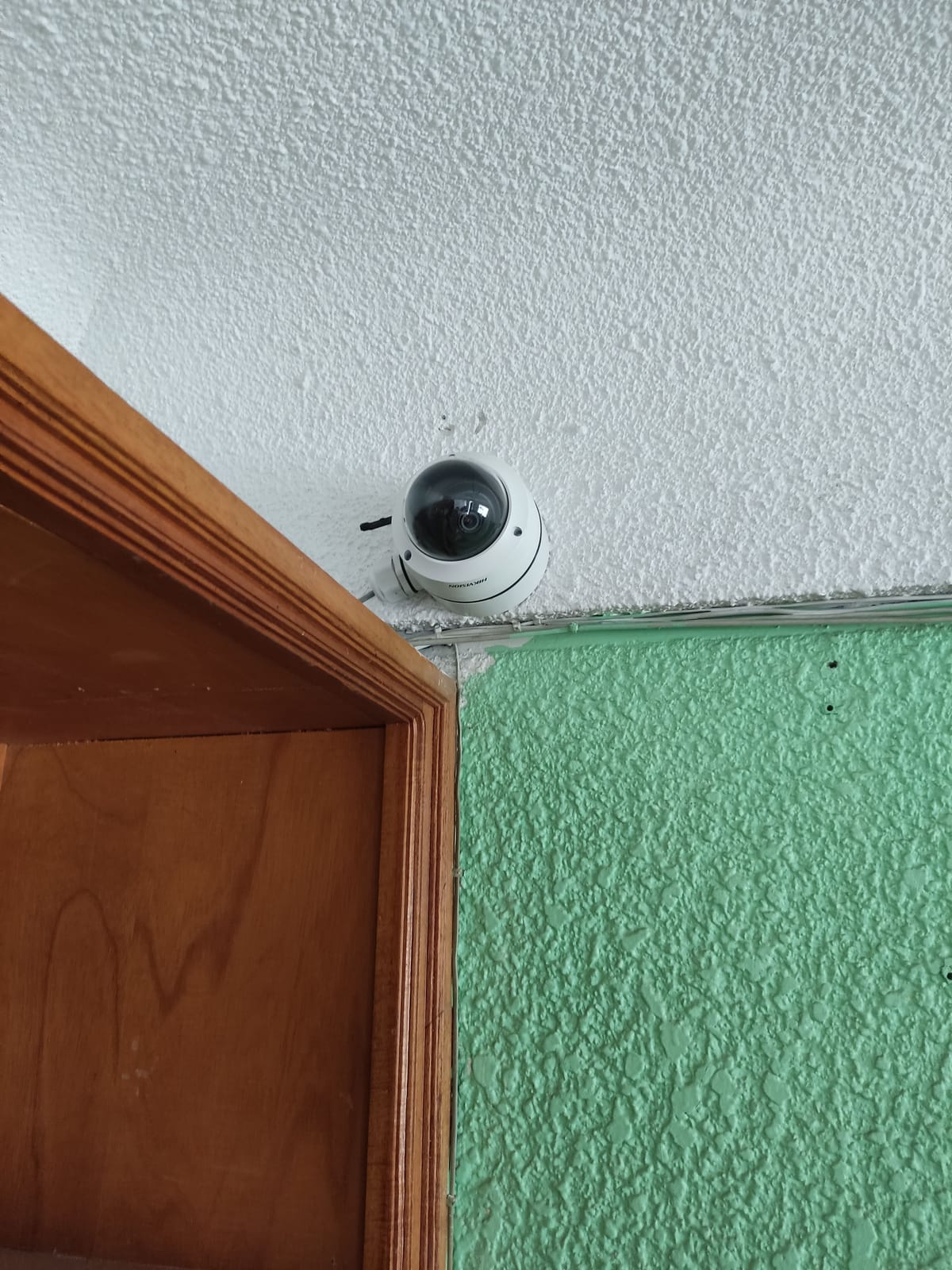 Domo Hikvision en esquina interior entre muro blanco y verde con zócalo de madera