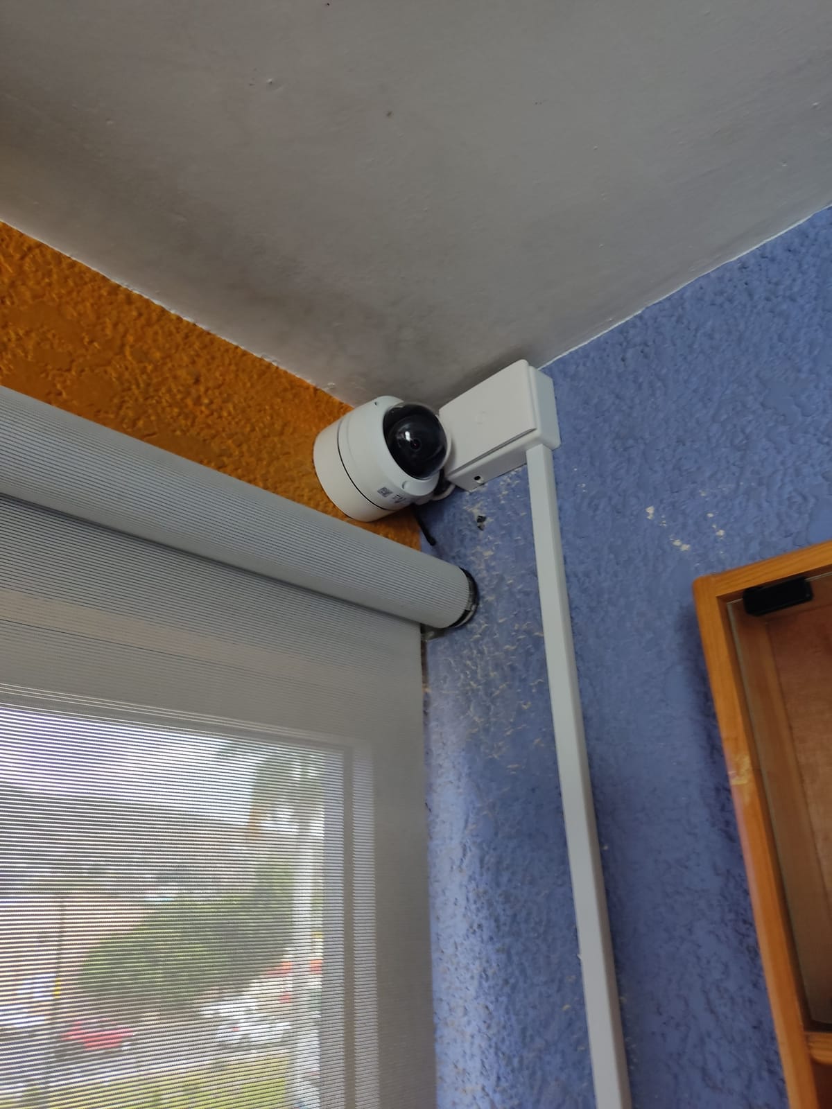 Mini PTZ Hikvision con soporte en esquina junto a ventana con persiana
