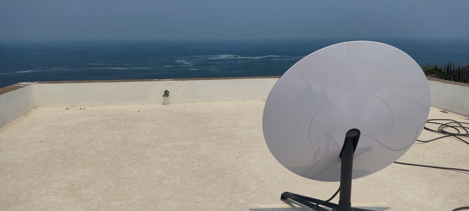 Antena satelital Starlink montada sobre trípode en una azotea con el mar de fondo