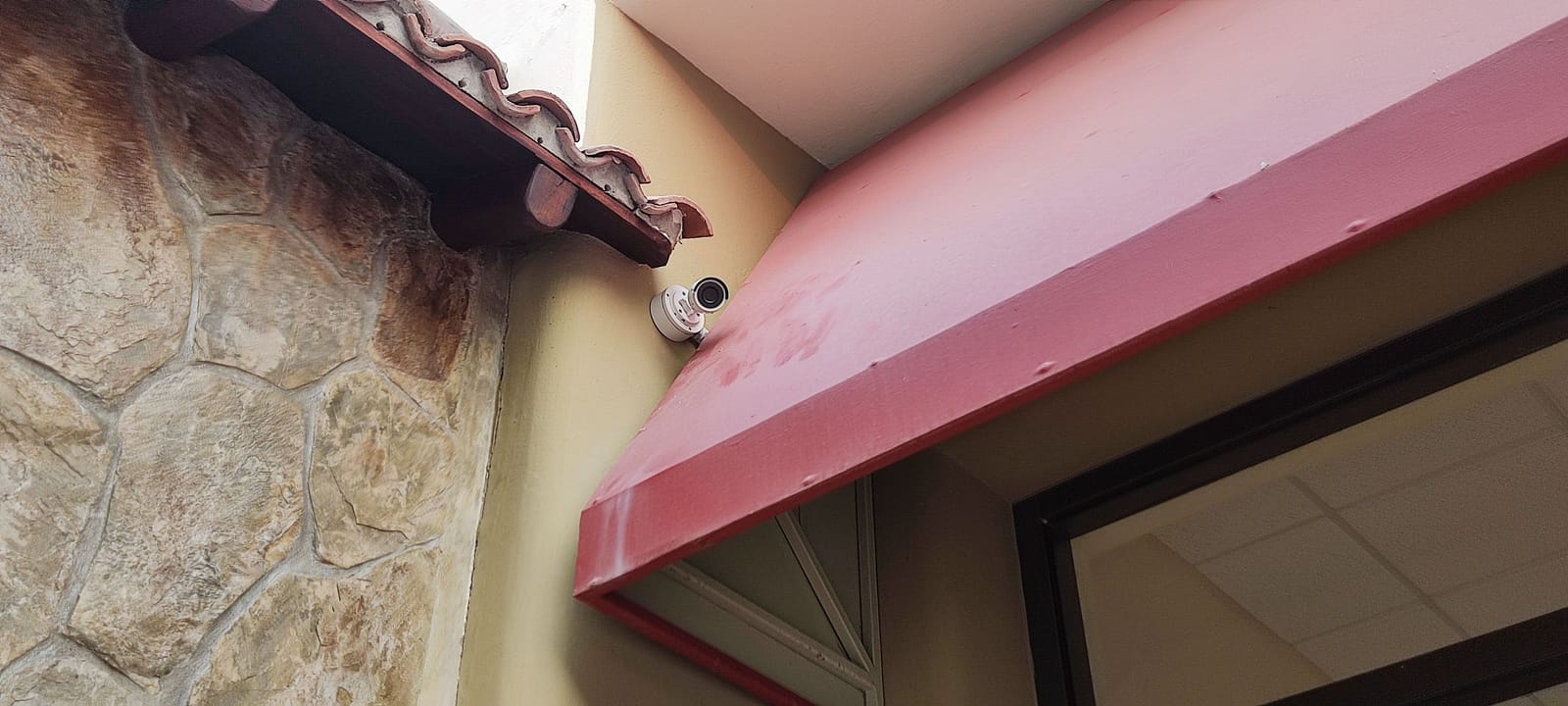 Cámara tipo bala instalada en una fachada de piedra bajo un alero de teja