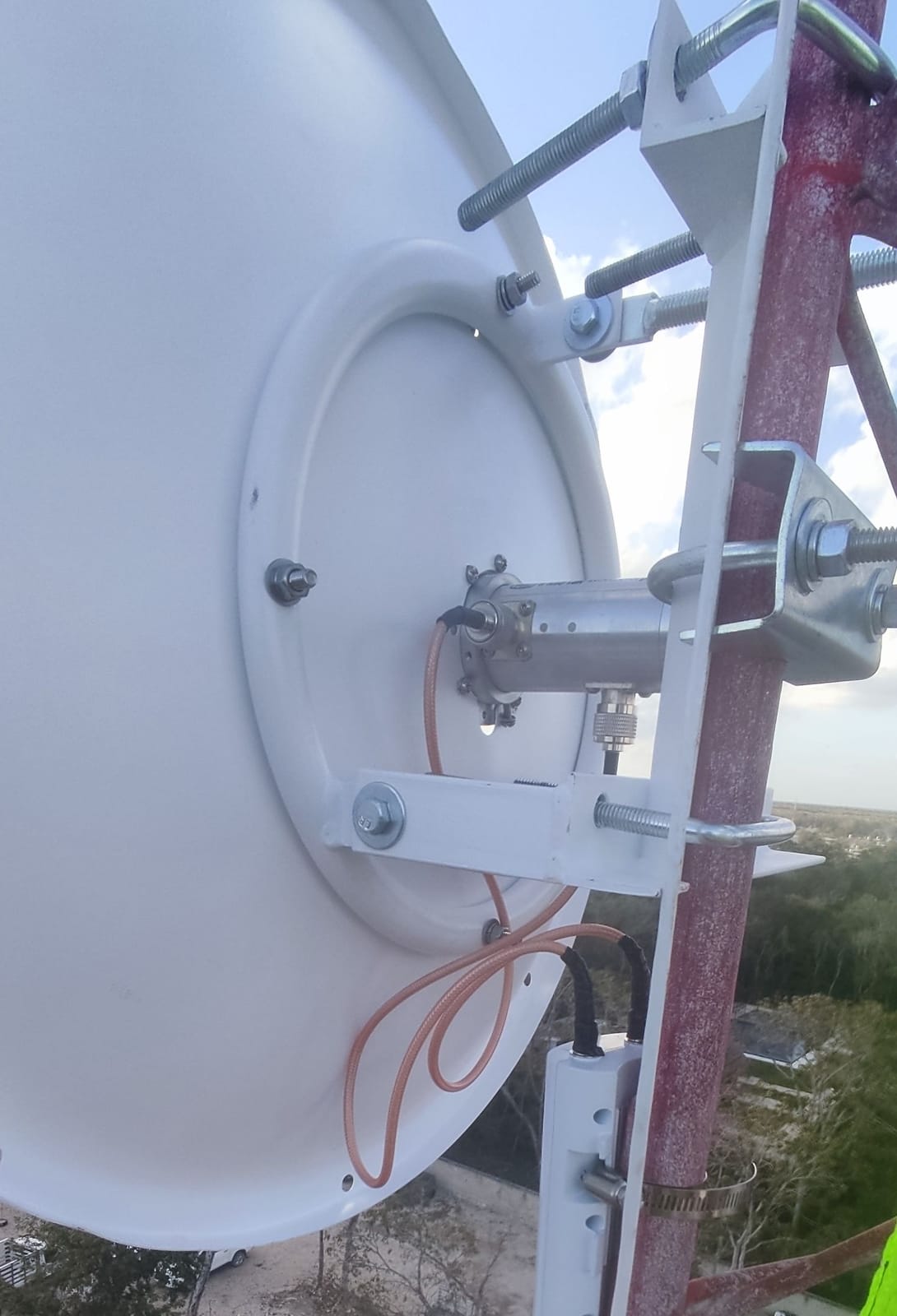 Parte trasera de una antena parabólica instalada en torre, con soporte de montaje, jumper coaxial y protección contra descargas