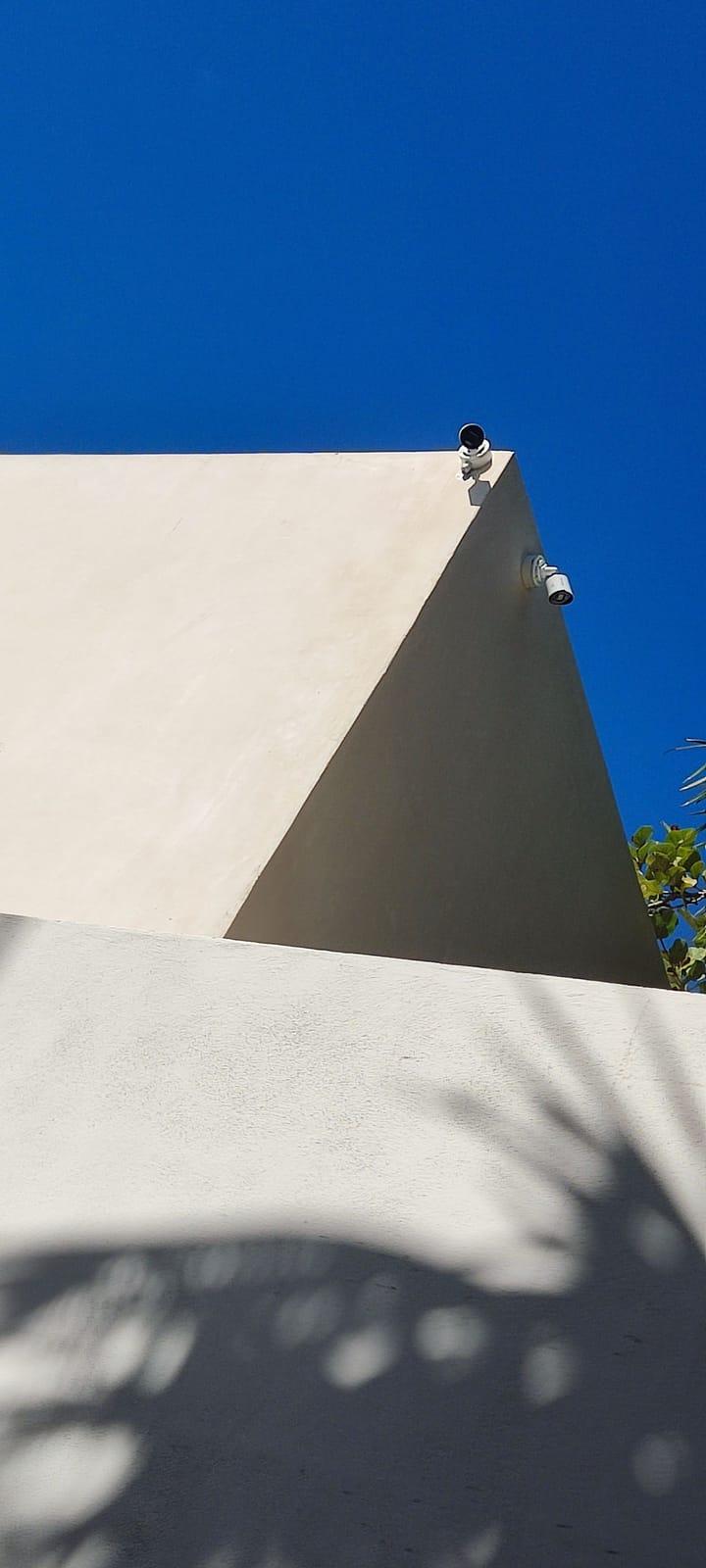 Cámaras bala Hikvision montadas en la esquina de un parapeto de estuco blanco contra un cielo azul