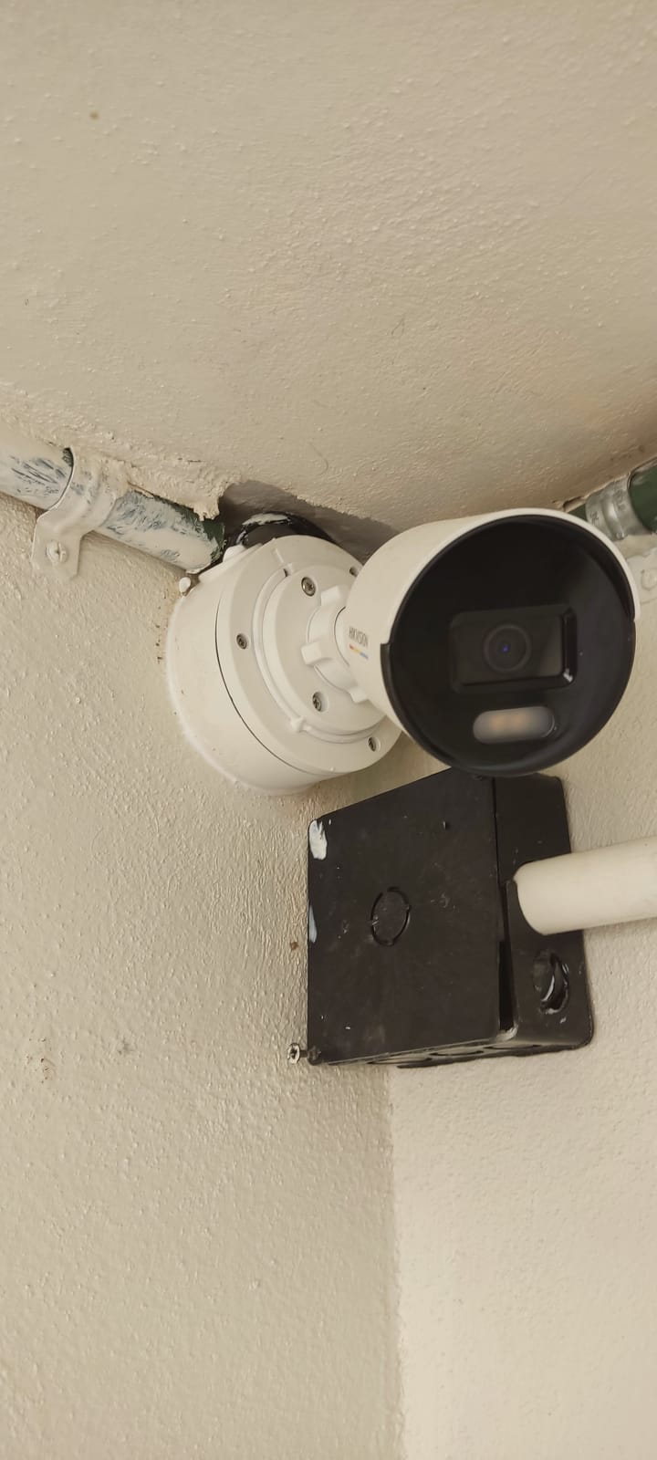 Cámara Hikvision ColorVu junto a una caja de registro y tubería en la unión de muro y techo