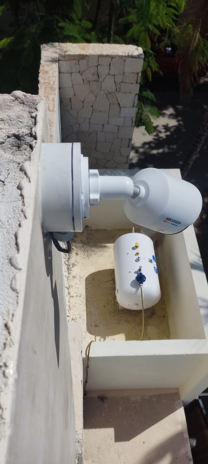 Cámara Hikvision sobre base circular en el borde de un muro de piedra rodeado de vegetación